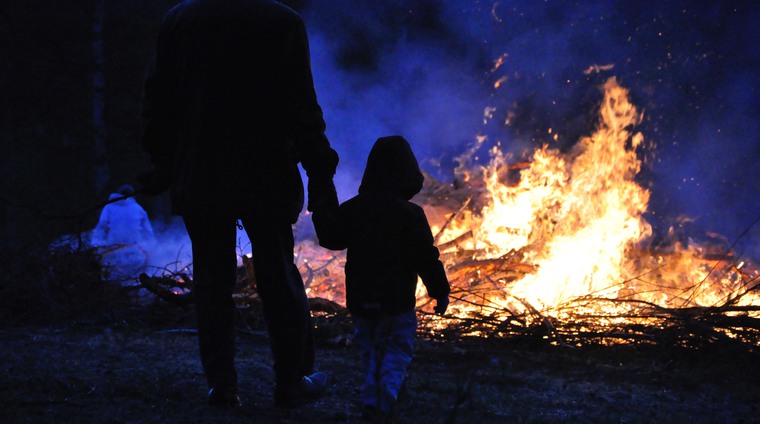 En vuxen håller ett barn i handen framför en brinnande majbrasa