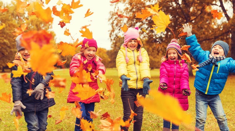 Fyra färgglada barn kastar höstfärgade löv i luften 